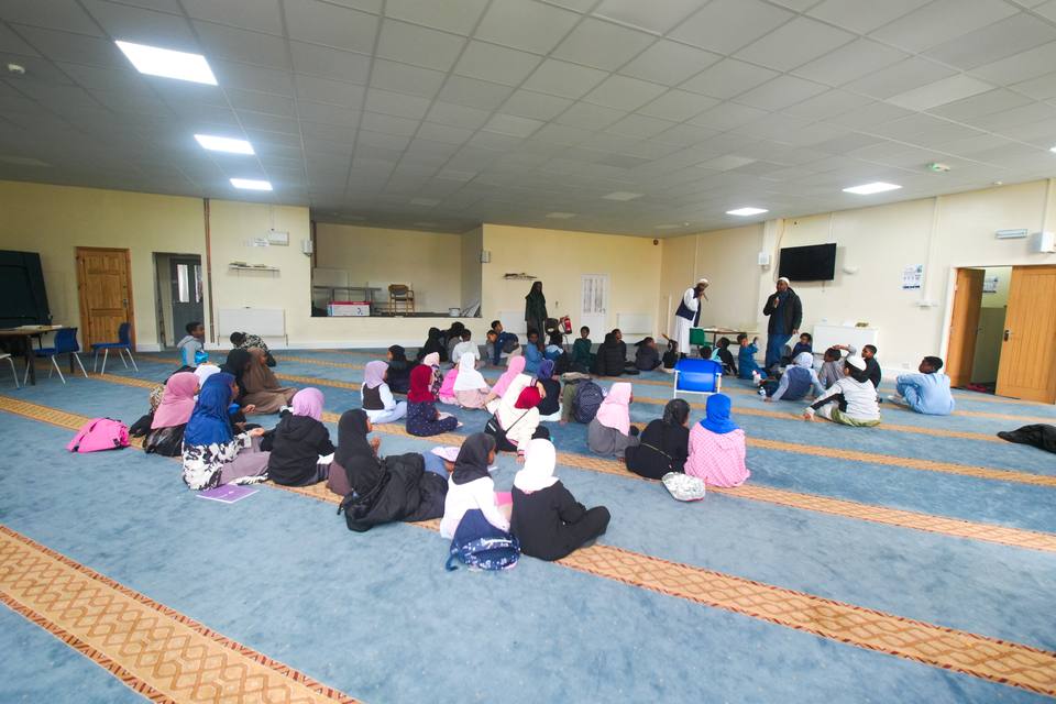 A children's class sitting on the blue carpet of the large hall