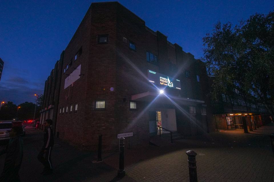 The masjid at dusk, a floodlight shining beside the entrance