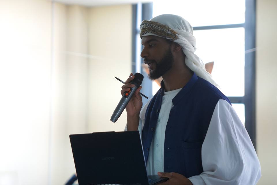 A teacher speaking into a microphone, a laptop in his other hand