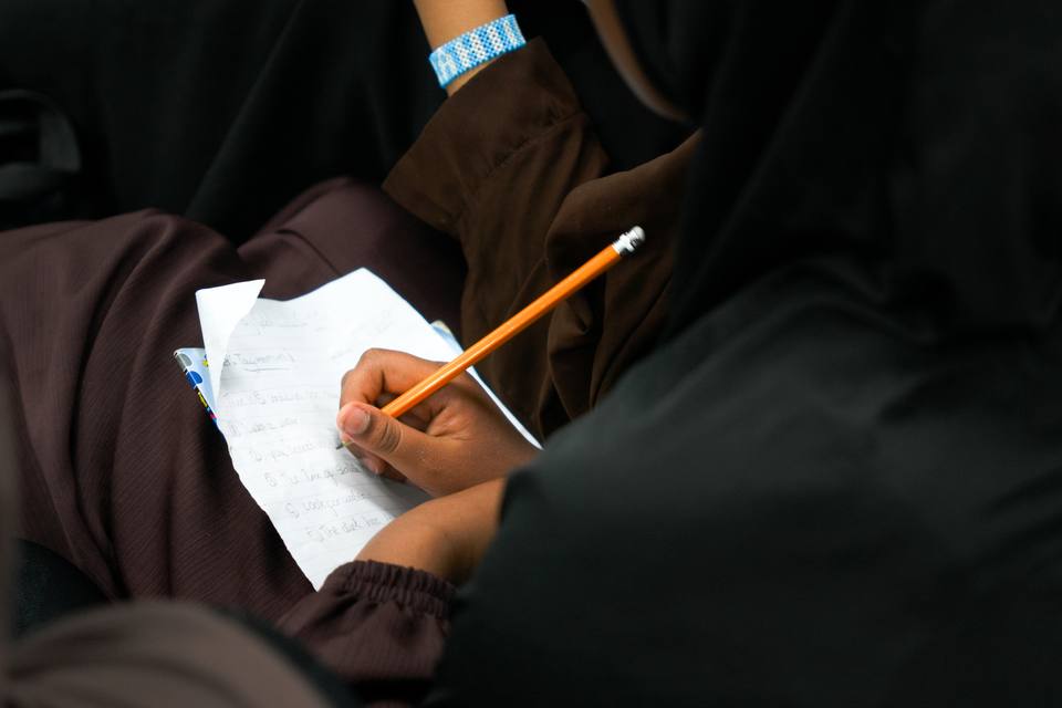 A hand writing notes in pencil on a sheet of paper