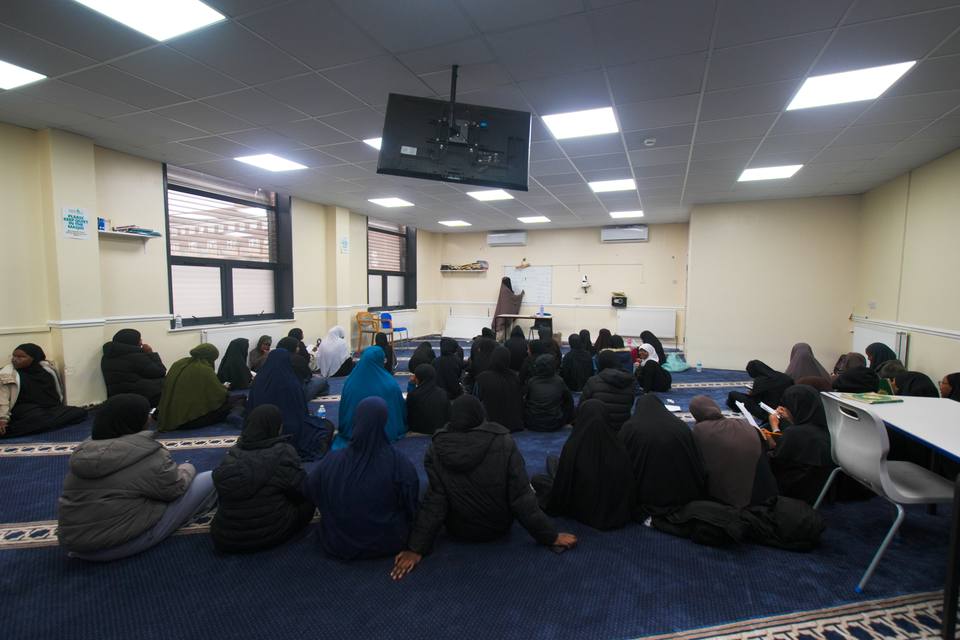 The sisters' class seated on the carpet facing their teacher