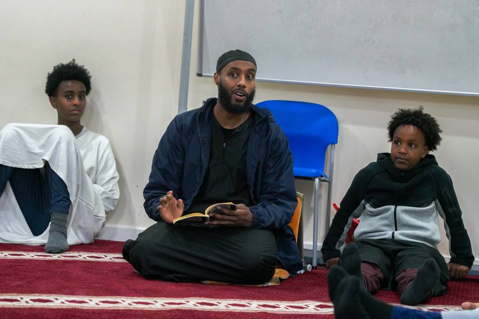 The teacher sitting on the carpet between two boys
