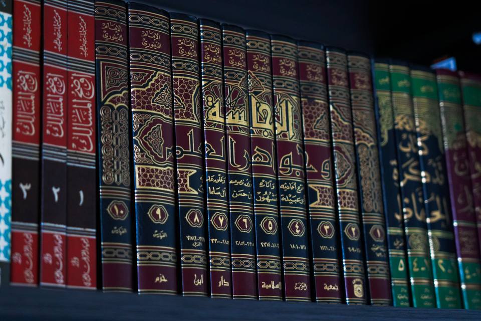 A row of red and gold bound volumes, their spines lettered in Arabic