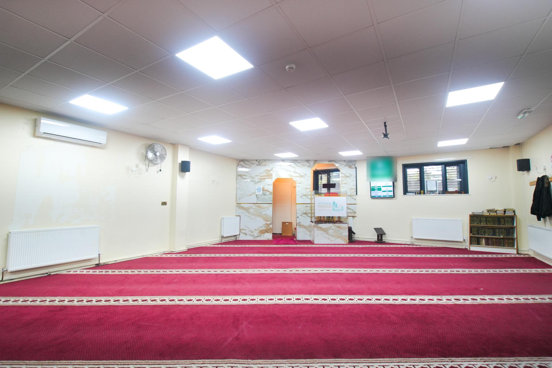The prayer hall, empty: red carpet in rows leading to a marble wall around the mihrab