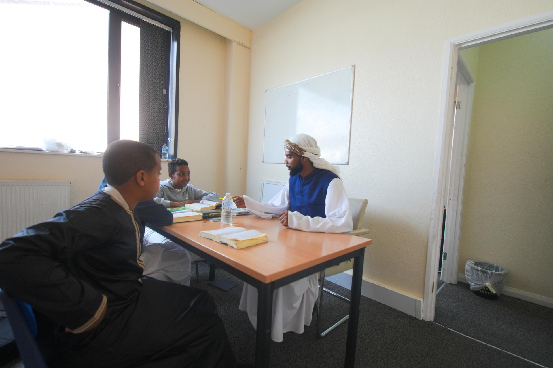 A teacher at a table with two boys, one reading to him